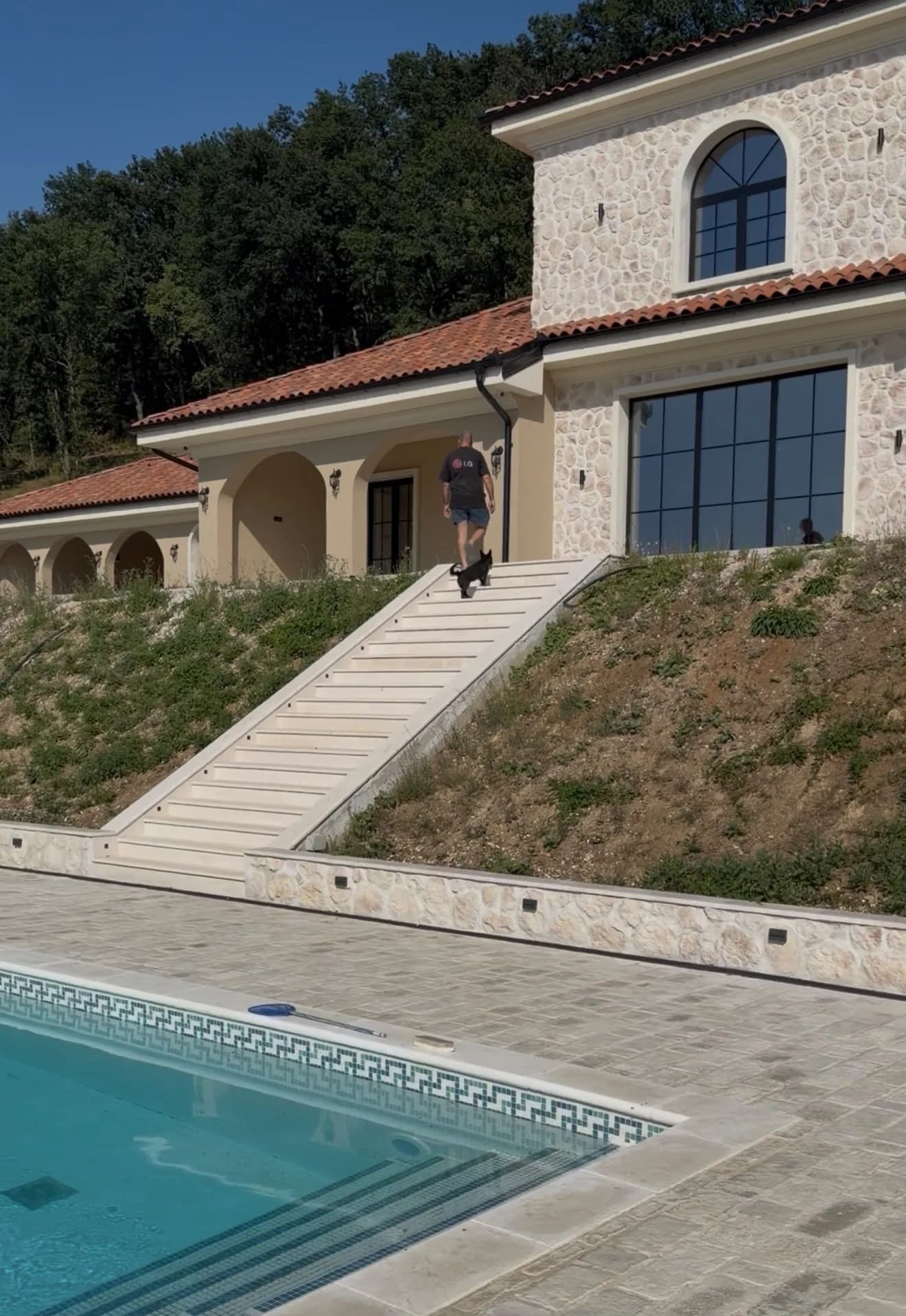 Vila sa svetlom kamenom fasadom, terasom i bazenom u podnožju stepeništa